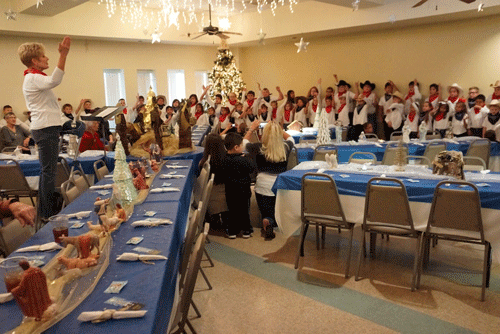 Judy Anderson leads the Port O’Connor School children in their Christmas musical presentation at the Annual Senior Citizens Christmas Luncheon. -Photo by Bill Tigrett
