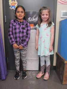 In POC Kindergarten class, Samary Garica and Vivian Kipp stand next to a picture of an Emperor Penguin to see if they are taller, shorter, or the same height as the penguin.