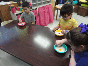 Students at POC kindergarten try to recreate what the milky way looks like by using milk, food coloring, and a Qtip. Left to right-Osvin Guiterrez, Andrew Martinez, and Alexis Taylor.