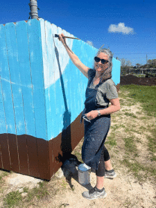 Dawn Ragusin painting a mural on the Community Garden fence.