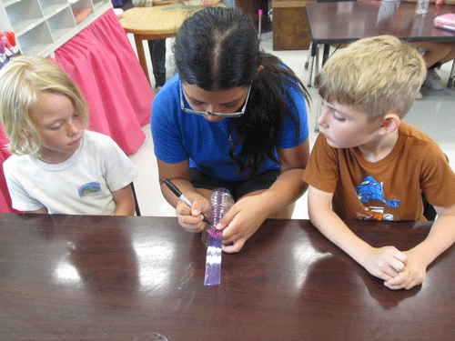 Jagger Tubbs (left) and Dean Bell (right) watch Saydi Ramerez help the two boys make a rain gauge to take home.